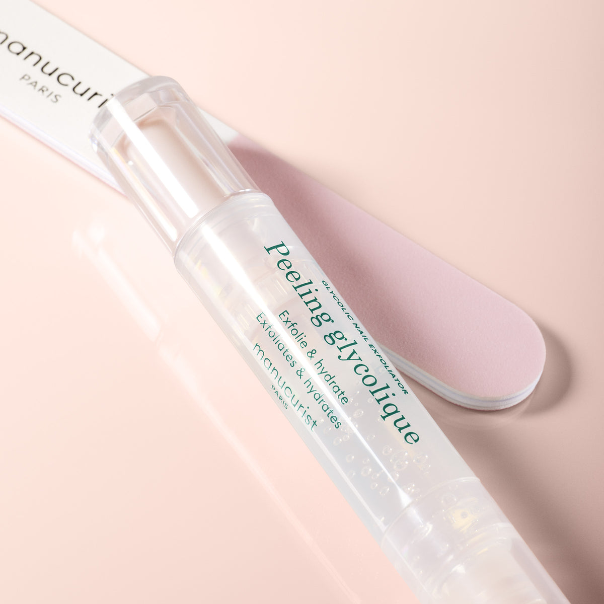 A clear, pen-shaped Prep Glow Routine by Manucurist rests on a pink surface beside a light pink nail file—ideal for exfoliating and hydrating nails and cuticles to achieve glossy nails in your care routine.