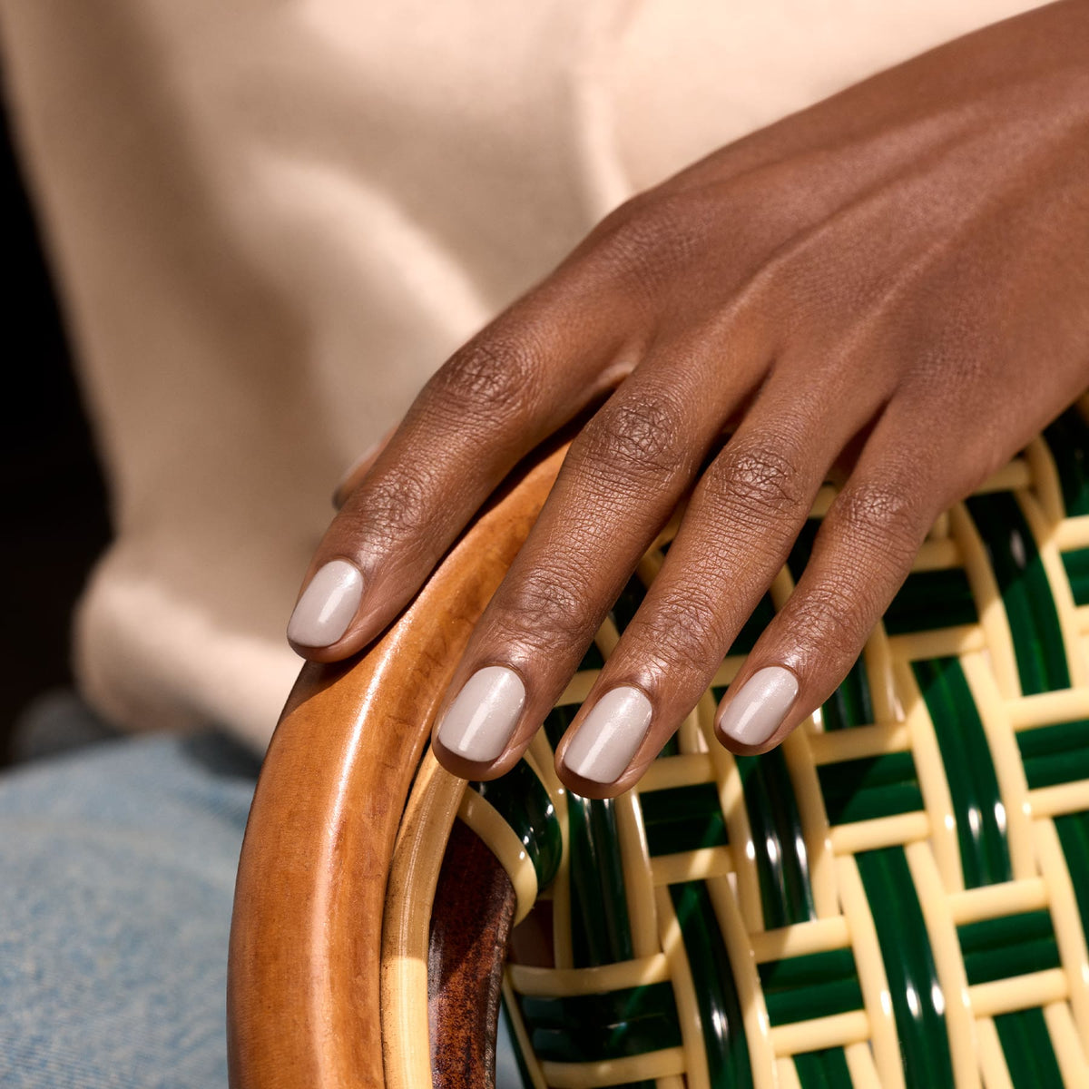 Une main aux ongles beige clair soigneusement manucurés, vernis avec "Tweed" de Manucurist, repose sur l&