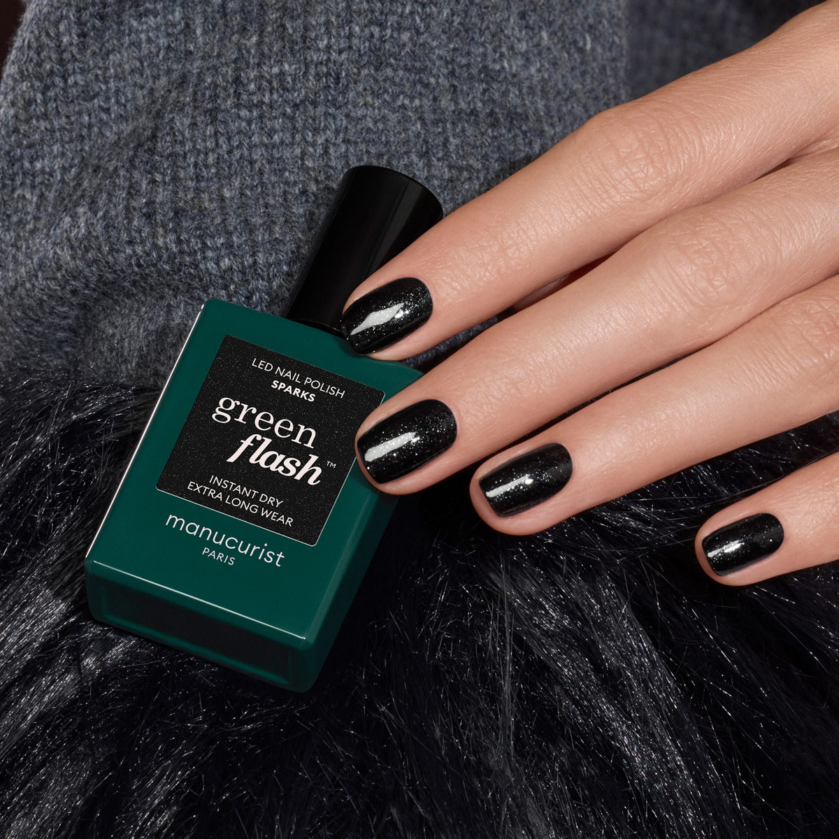 Une main aux ongles courts et brillants avec un vernis gel pailleté noir repose à côté d&