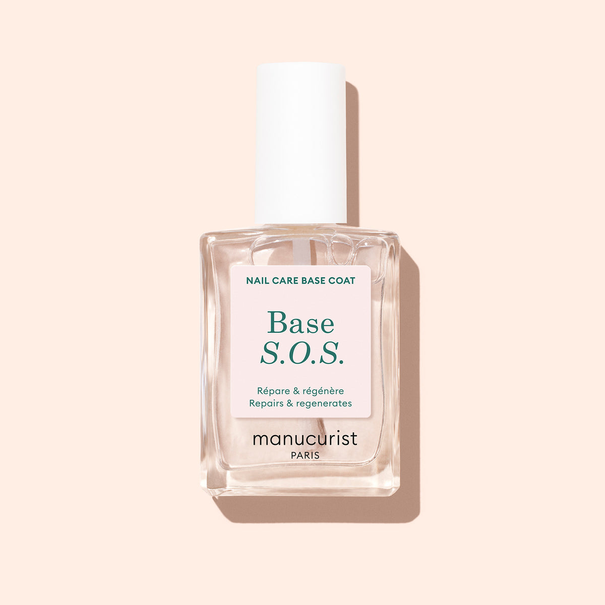 A clear Manucurist S.O.S. Nail Strengthener bottle with a white cap sits on a light beige background, featuring a label in French and English stating "Repairs regenerates"—perfect for brittle nails needing repair.
