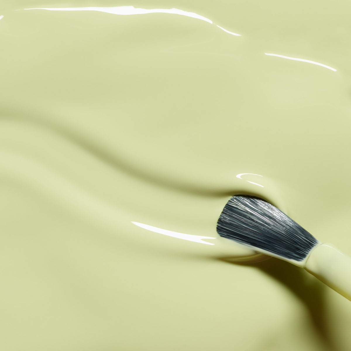 Un pinceau repose sur la surface lisse et brillante de la teinte Pistachio de Manucurist — un vert clair tirant sur le jaune aux ondulations subtiles — évoquant le look pastel et doux de ce vernis LED Gel.