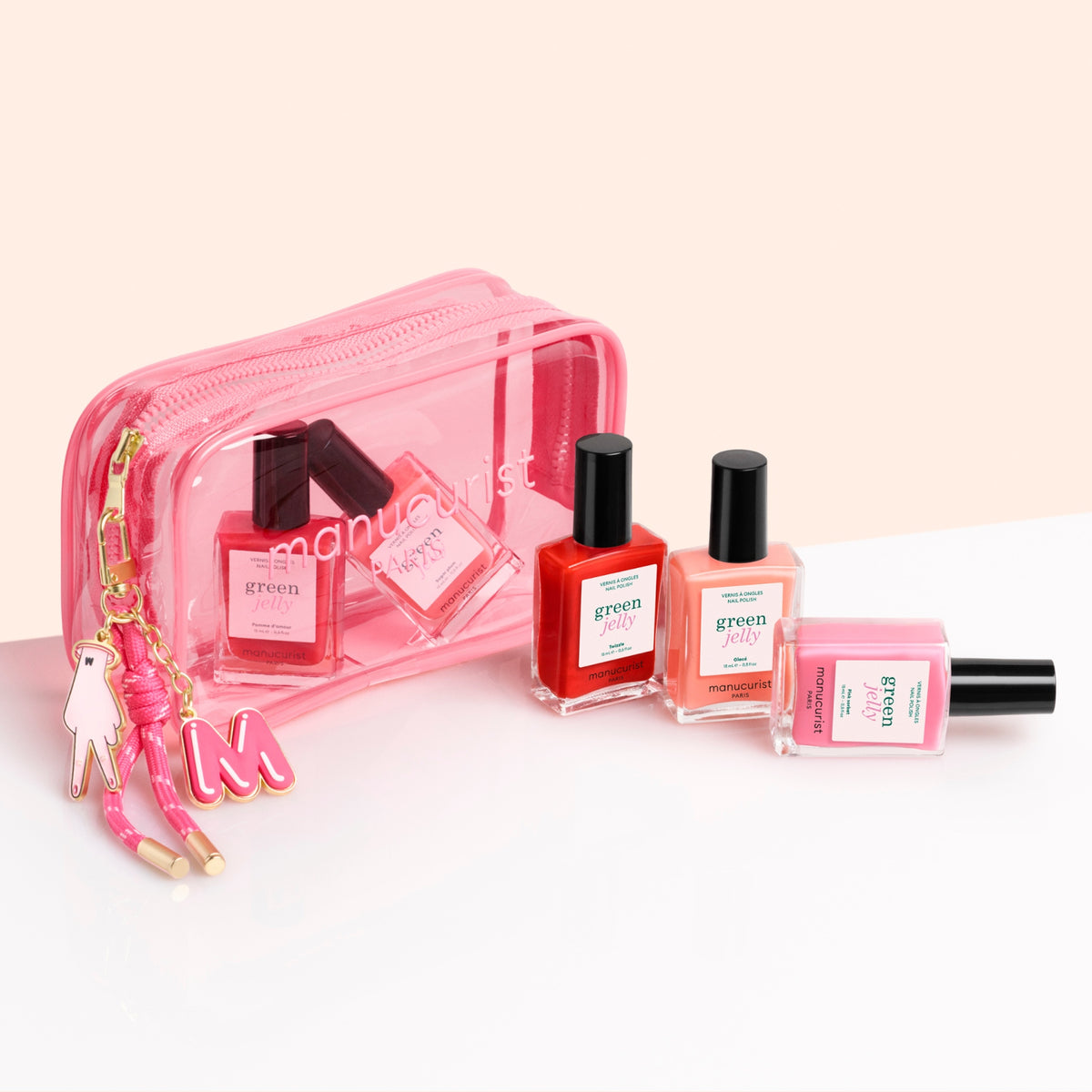 Trois flacons de vernis à ongles rose, orange et transparent sont posés devant la pochette Manucurist Jelly Summer Pouch — une trousse transparente ornée d&