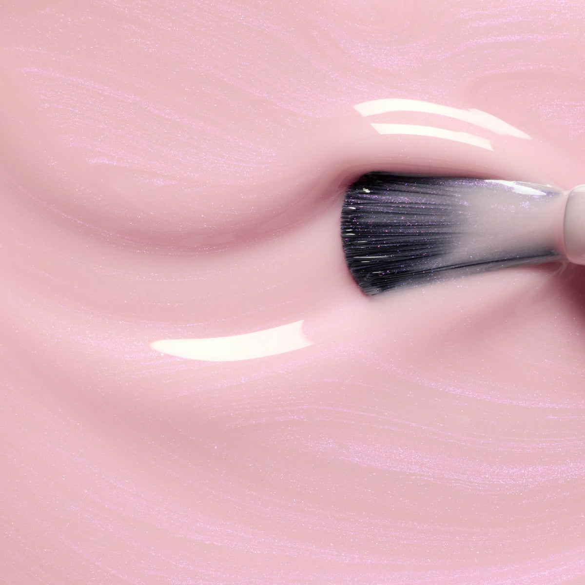 Gros plan sur un pinceau de maquillage tournoyant dans Halo de Manucurist, un vernis gel rose clair brillant, créant de douces textures ondulées et des reflets lumineux.