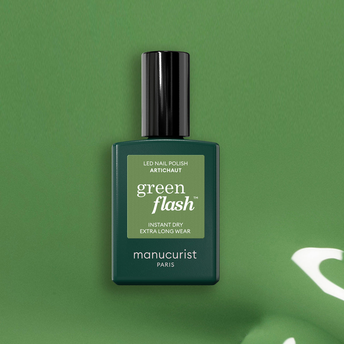 Un flacon de vernis LED Manucurist Artichoke Green Flash repose sur un fond vert assorti. Le flacon rectangulaire arbore un bouchon noir et un texte blanc, évoquant la fraîcheur luxuriante d&
