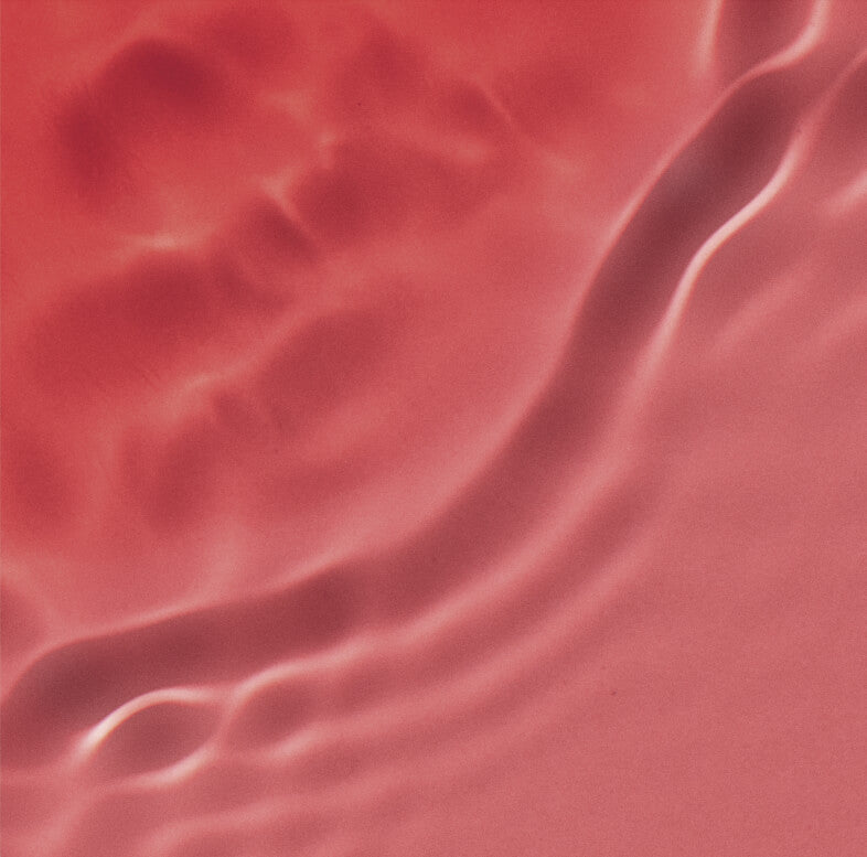 Abstract image with soft pink and red hues, featuring wavy, flowing textures and smooth, undulating patterns resembling ripples or sand dunes. The surface has a shiny, reflective quality.