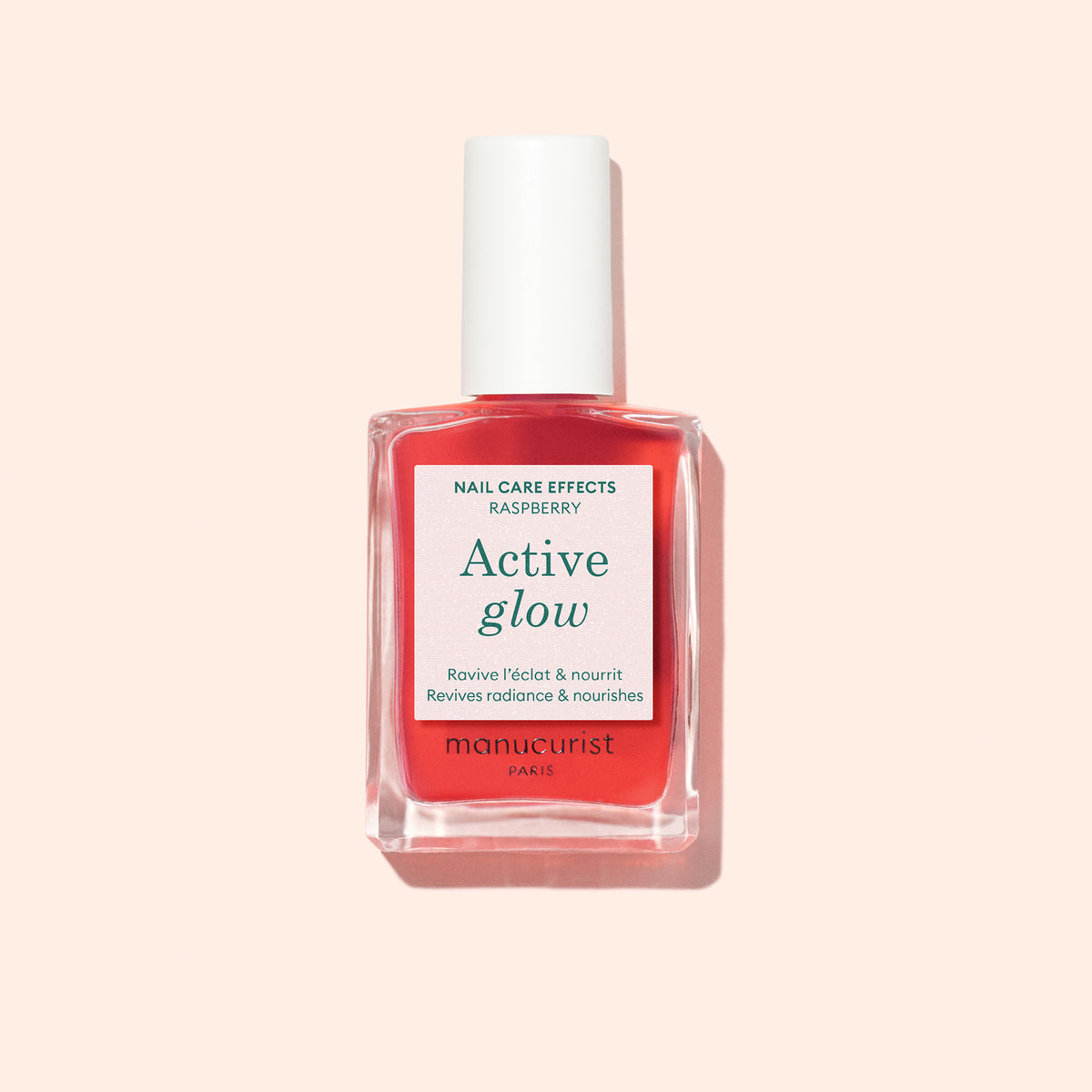 A bottle of Manucurist Active™ Glow Raspberry nail care polish, featuring a white cap and a pink label on a light peach background, provides plant-based nourishment for healthy, radiant nails.