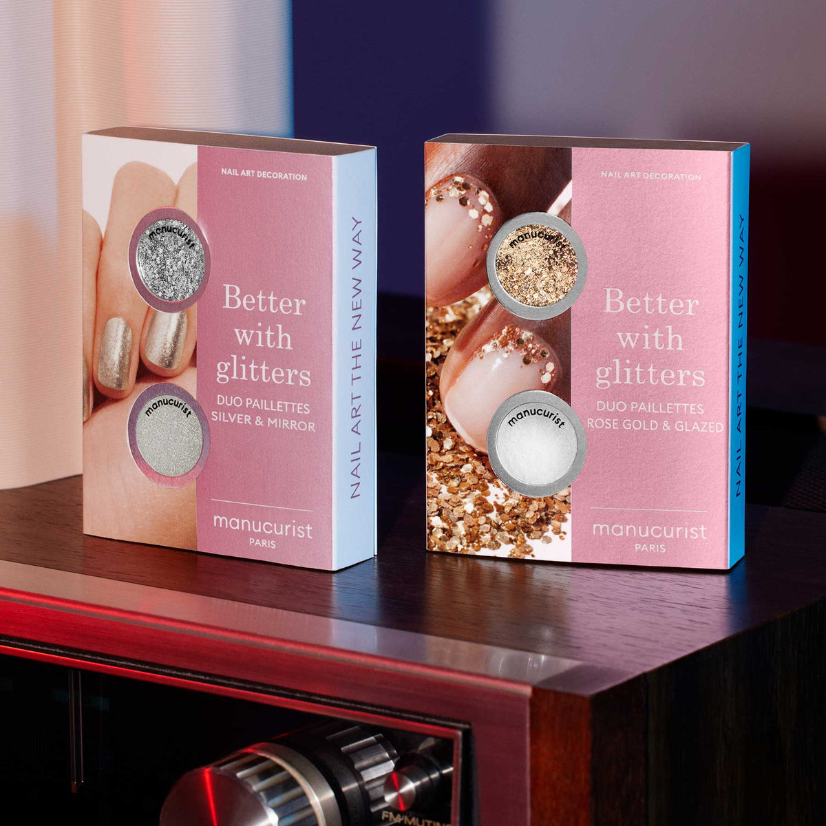 Two pink and white boxes of Manucurist Glitters Duo Silver Mirror sit side by side on a dark surface, each featuring nail designs with silver glitter, mirror effect powder, rose gold, and glazed shades.
