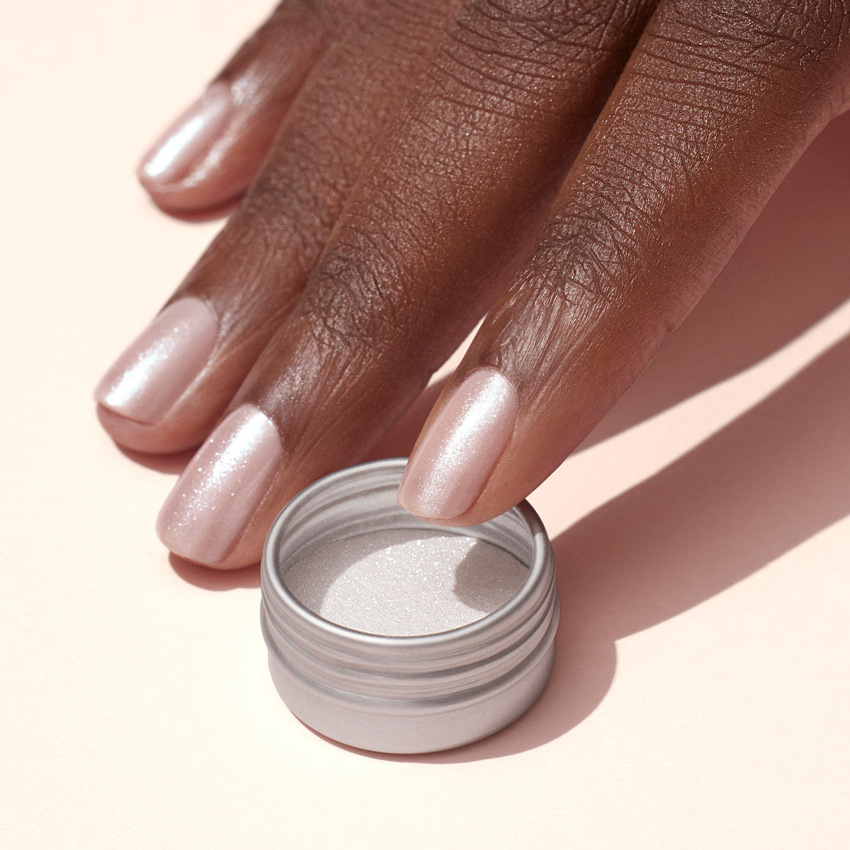 Une main aux ongles rose pâle et irisés arborant un subtil effet glazed blanc créé avec la Poudre Effet Glazed Blanc de Manucurist repose à côté d&