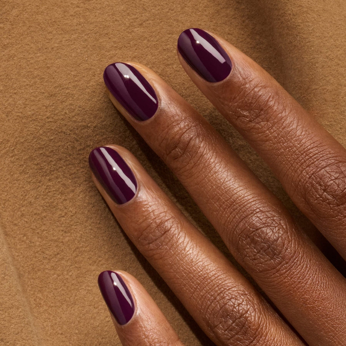 A close-up of a dark-skinned hand resting on brown fabric, featuring neatly manicured nails painted with Manucurist&
