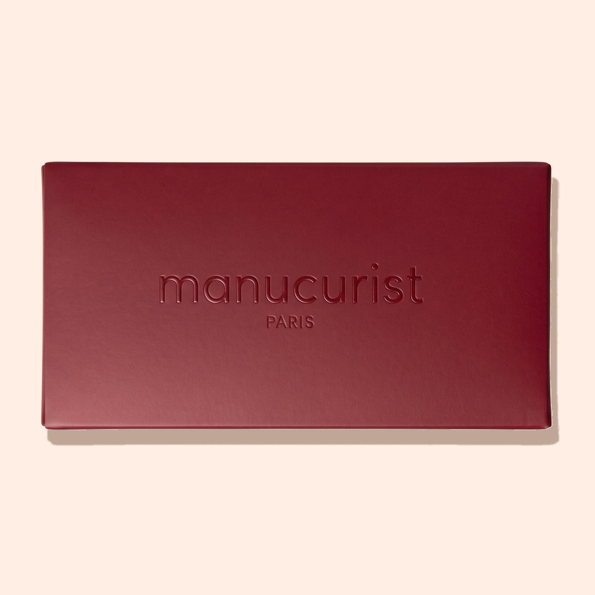 Un coffret rectangulaire fermé Holiday Rainbow Burgundy par Manucurist, avec le nom de la marque et « PARIS » embossés sur le couvercle, sur un fond beige clair.