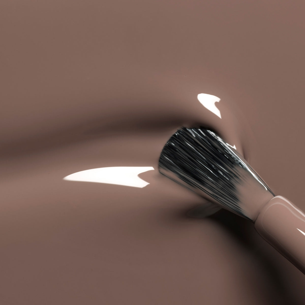 A close-up of a makeup brush gliding glossy nude foundation with smooth ripples—pair it with Manucurist&