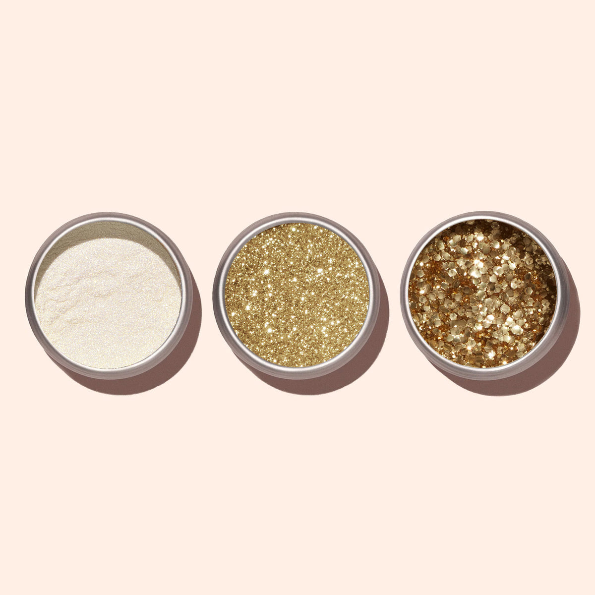 Three Manucurist Gold Biodegradable Glitter pots, ideal for nail art, are arranged in a row on a pale beige background.