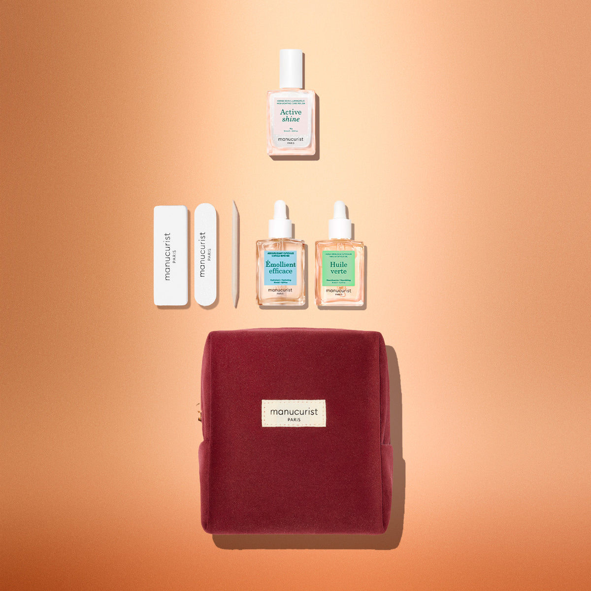 The Manucurist Active™ Discovery Gift Set is beautifully displayed on a peach background and features a red velvet pouch, nail files, cuticle pusher, two bottles of nail care oil, and a bottle of nail serum—all perfectly arranged. This set makes an ideal holiday gift for anyone who loves a relaxing manicure routine and gorgeous nails.