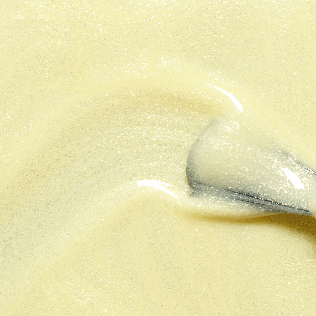 A close-up of a spoon stirring creamy, pale yellow batter—evoking the soft hue of Lemonade nail polish from the Manucurist Green™ range.