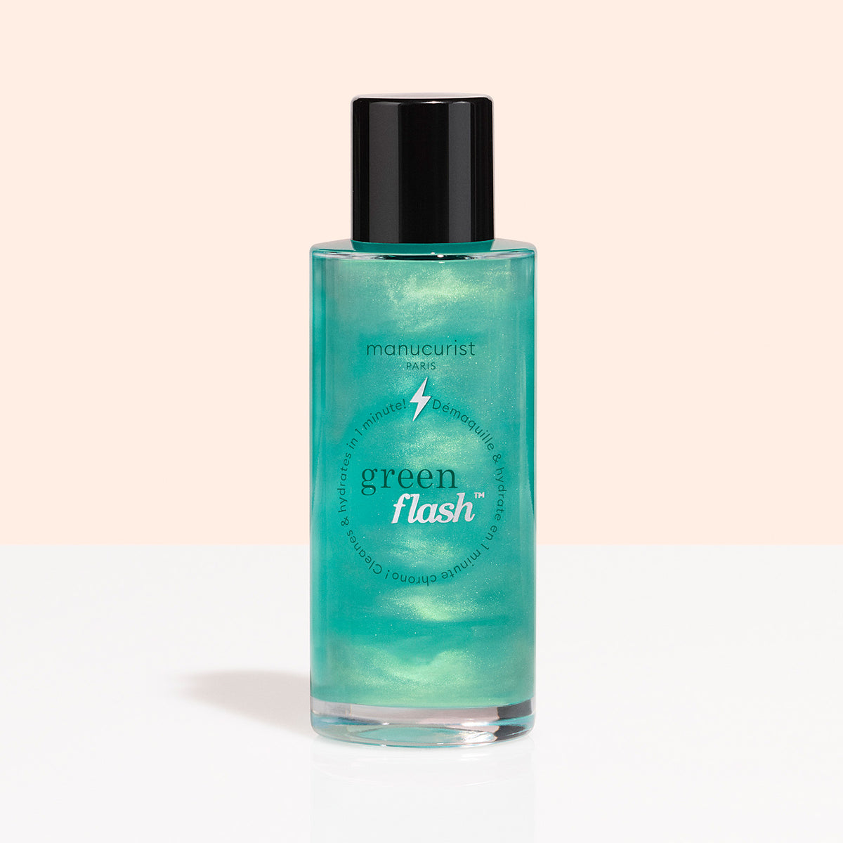 Un flacon transparent avec un bouchon noir, étiqueté « Manucurist Green Flash™ Gentle Glitter Remover », contient un liquide bleu sarcelle scintillant, sans acétone, et est présenté sur un fond pêche clair et blanc.