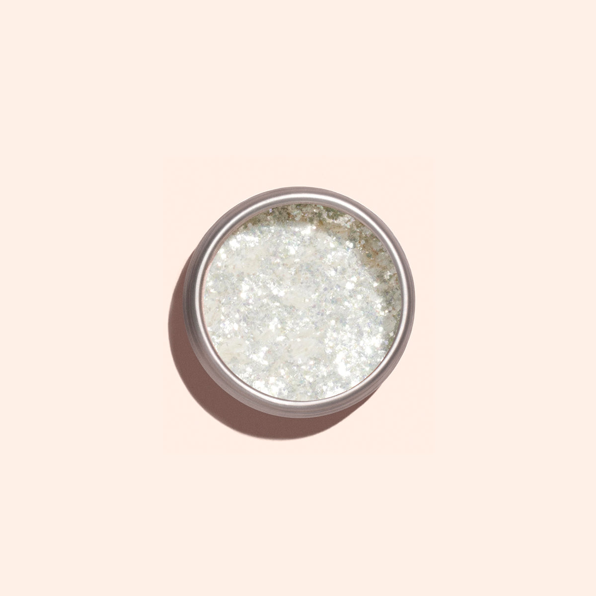 Les flocons de paillettes nacrées Manucurist se présentent dans un petit contenant rond sur un fond pêche pâle, projetant une ombre douce — idéal pour ajouter un éclat scintillant à votre prochaine manucure.