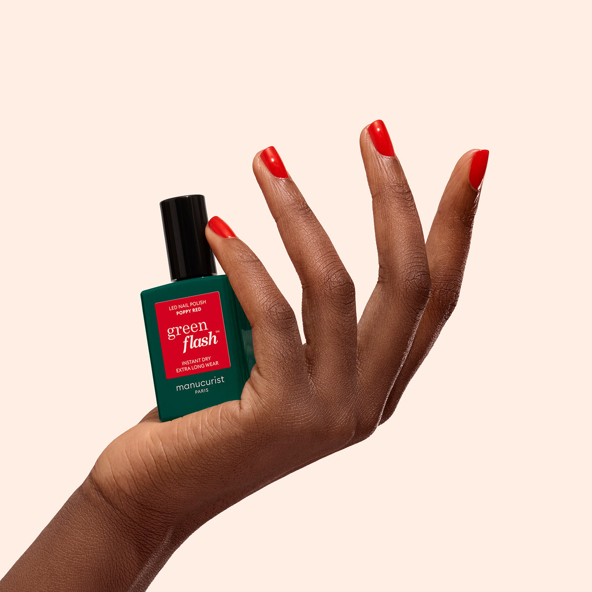 A hand with Poppy Red-painted nails holds a bottle of Manucurist&
