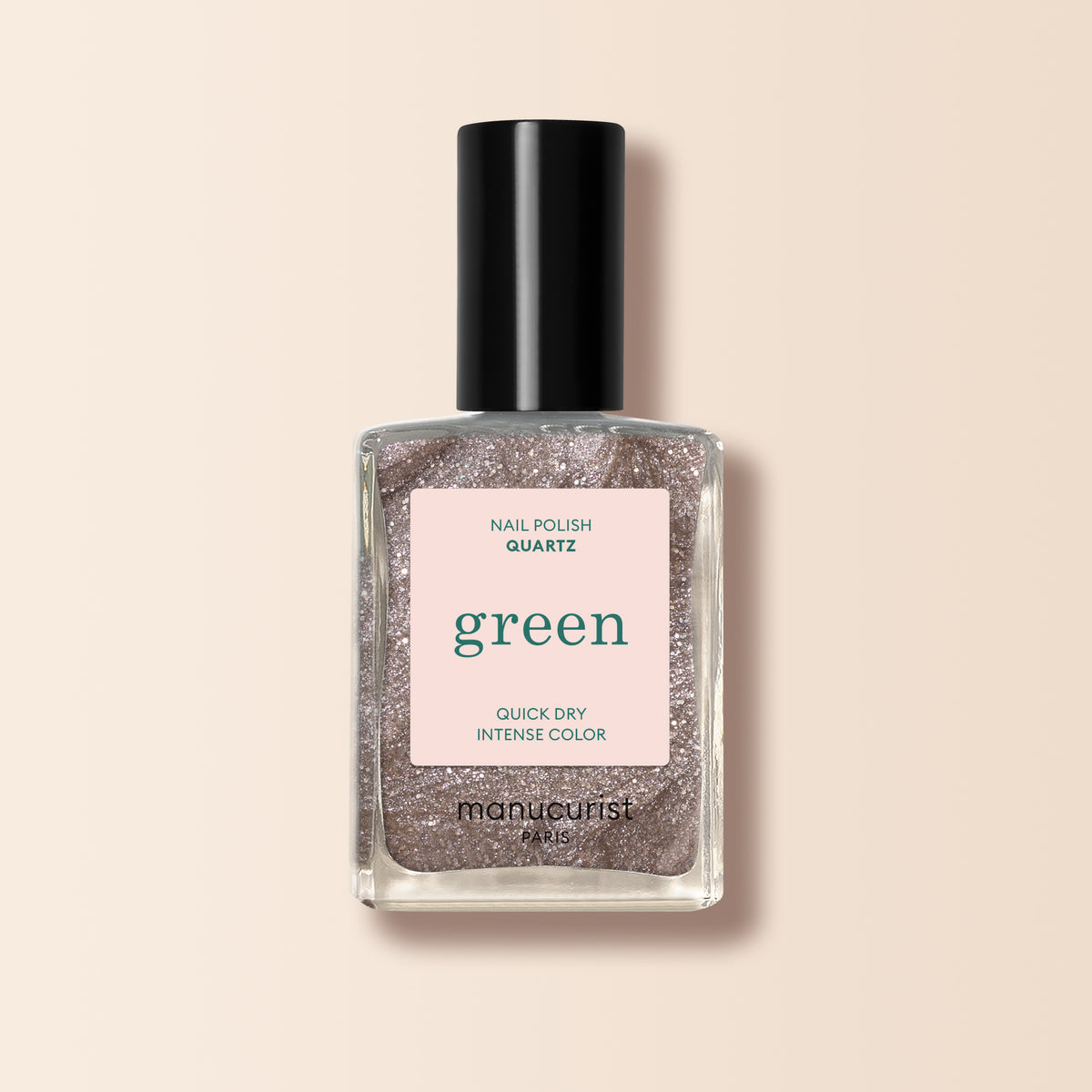 Un flacon transparent de vernis à ongles Manucurist Quartz avec un capuchon noir, présentant une teinte rose gold nacrée étiquetée « green » et « quick dry intense color » sur un fond beige doux.
