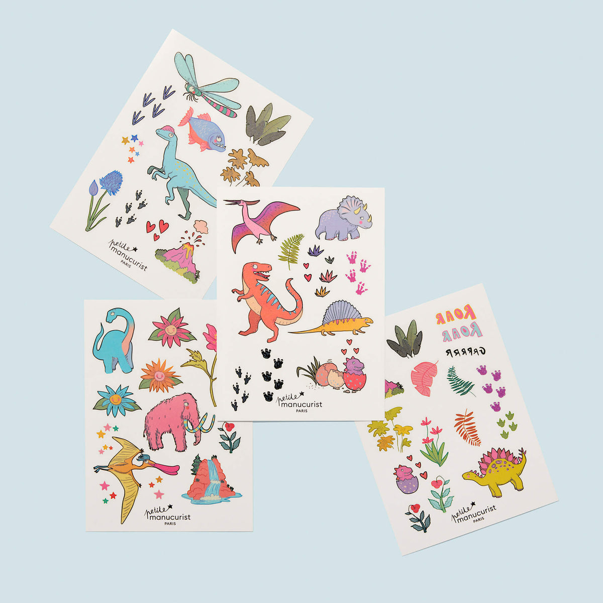 Quatre feuilles de tatouages Wild Life de Manucurist, parfaits pour la rentrée, représentant chacune des dinosaures en dessin animé colorés, des plantes, des fleurs et des empreintes de dinosaures sur fond bleu clair.