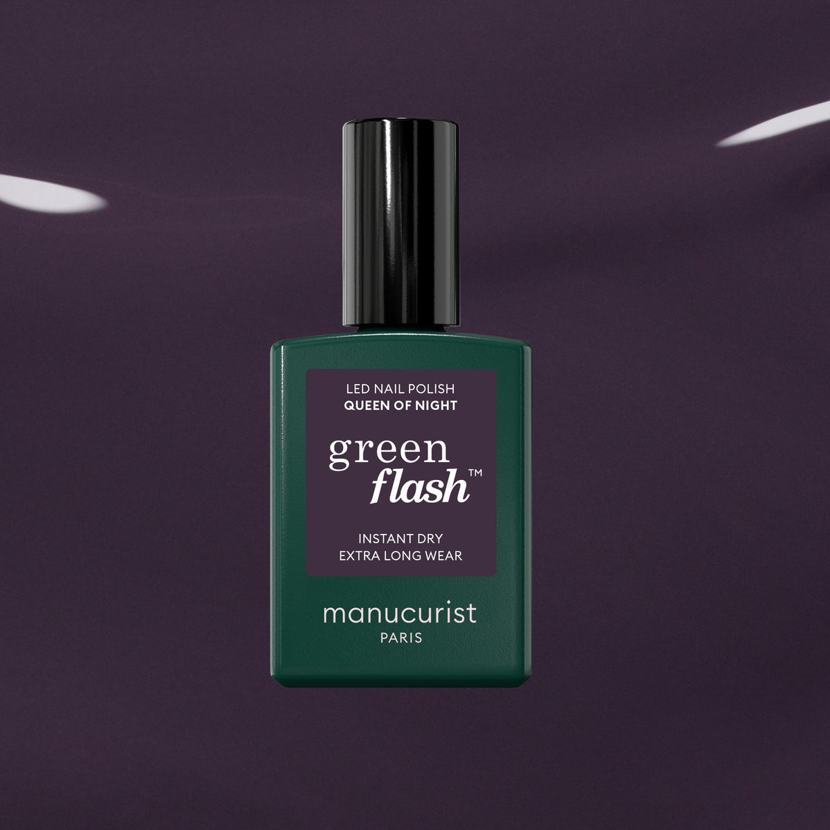 Un flacon de vernis à ongles Manucurist Queen of Night vert foncé repose sur un fond violet brillant, mettant en valeur ses sous-tons gris et son style unique.