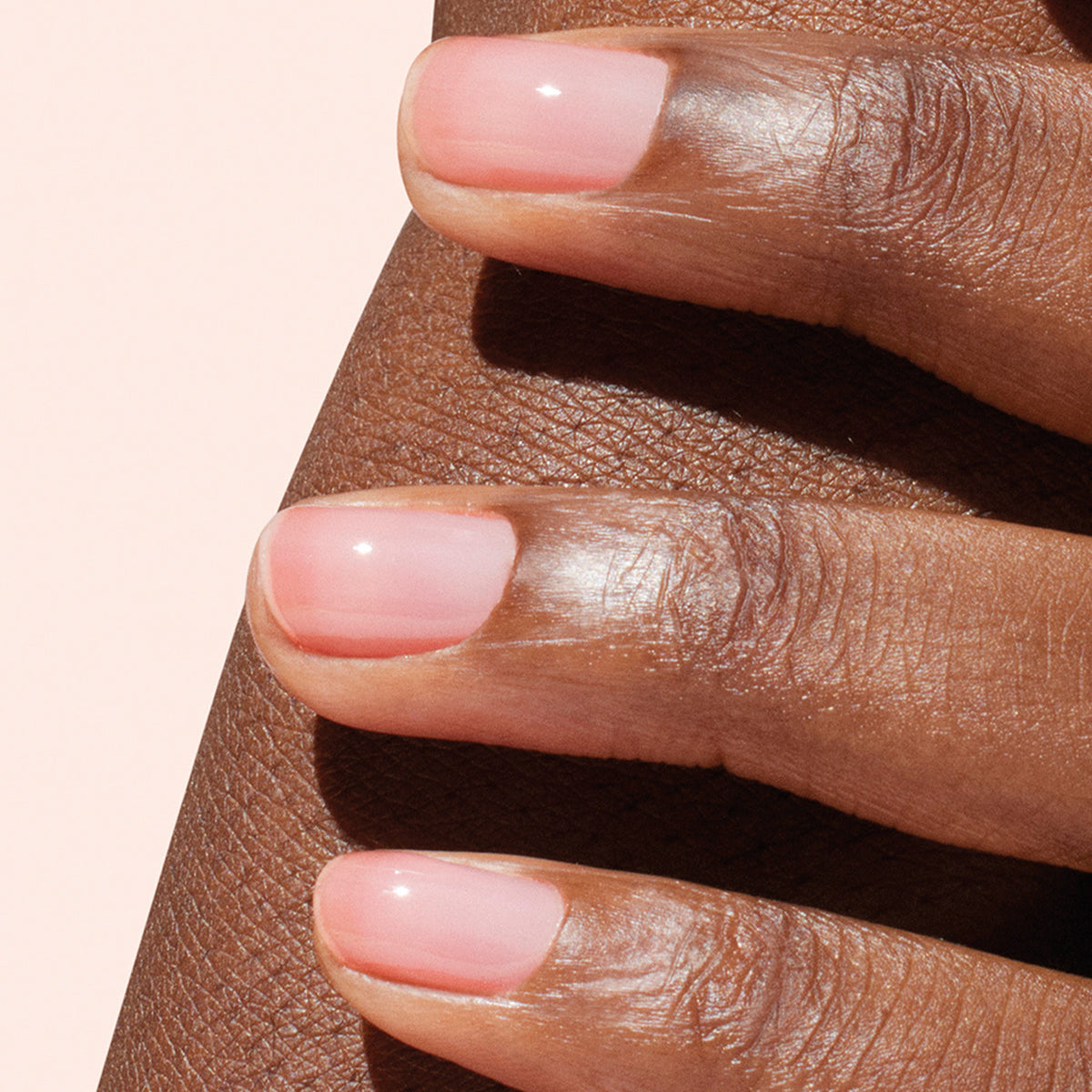 A close-up showcases a hand with neatly manicured nails painted in Manucurist’s Active™ Glow Raspberry—a light pink shade—resting gently against a medium to dark forearm. The glossy finish of the nails highlights careful nail care and nourishment.