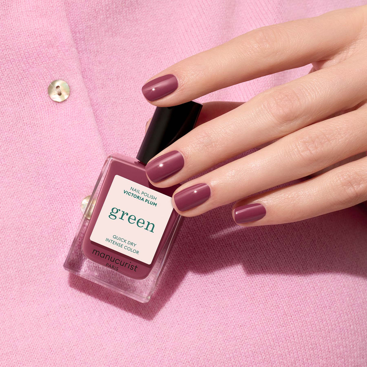 A hand with mauve nails holds a bottle of Manucurist&