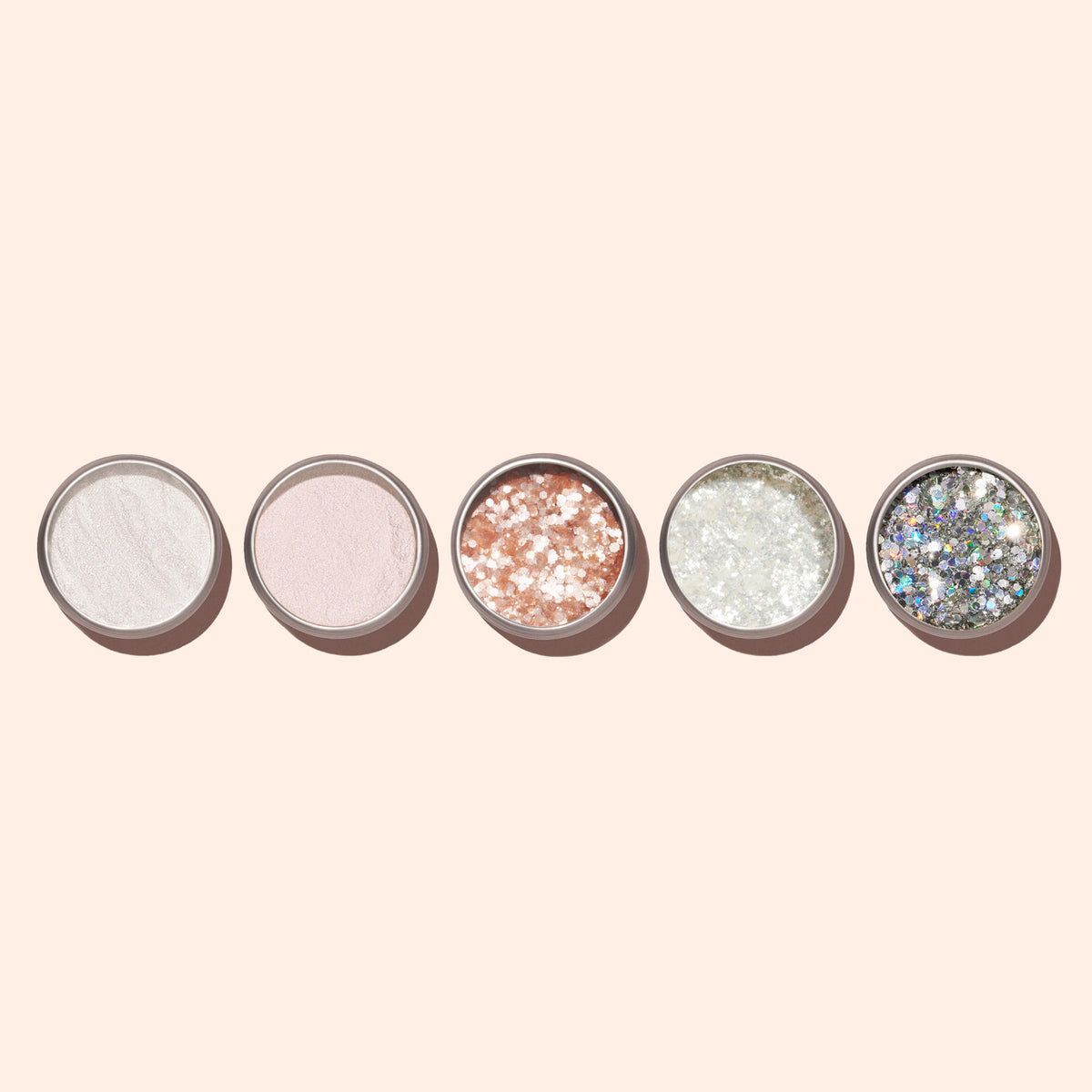 Cinq petits pots ronds de Paillettes Biodégradables Nacrées Manucurist, contenant chacun différentes teintes et textures de poudres scintillantes ou pailletées, sont alignés sur un fond beige clair.