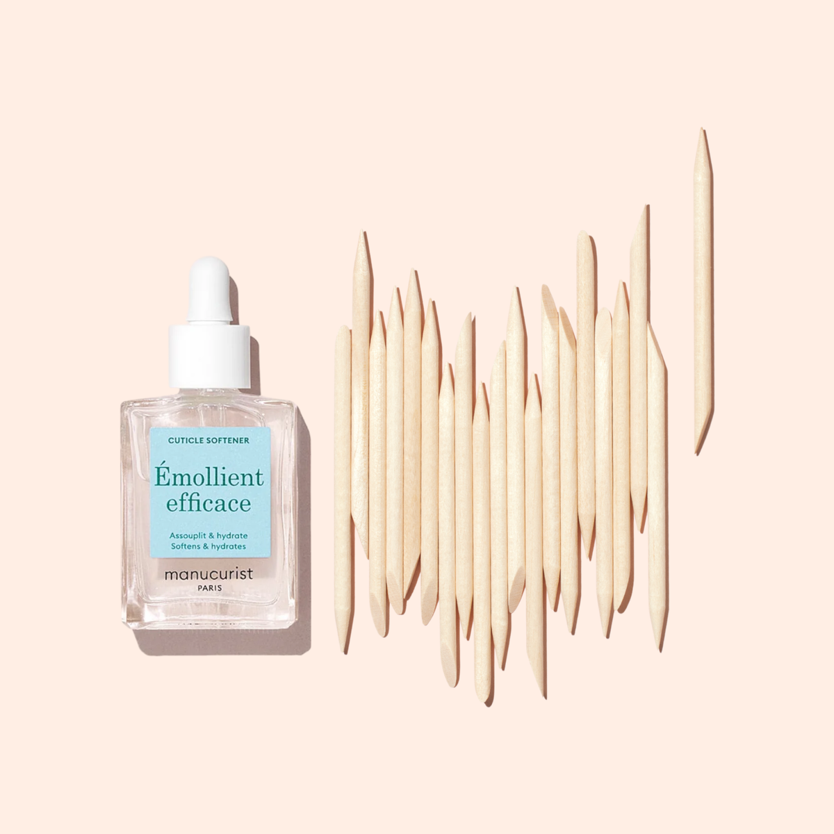 A Manucurist Wooden cuticle stick x20 set is arranged neatly next to a glass dropper bottle labeled Émollient efficace on a light beige background.