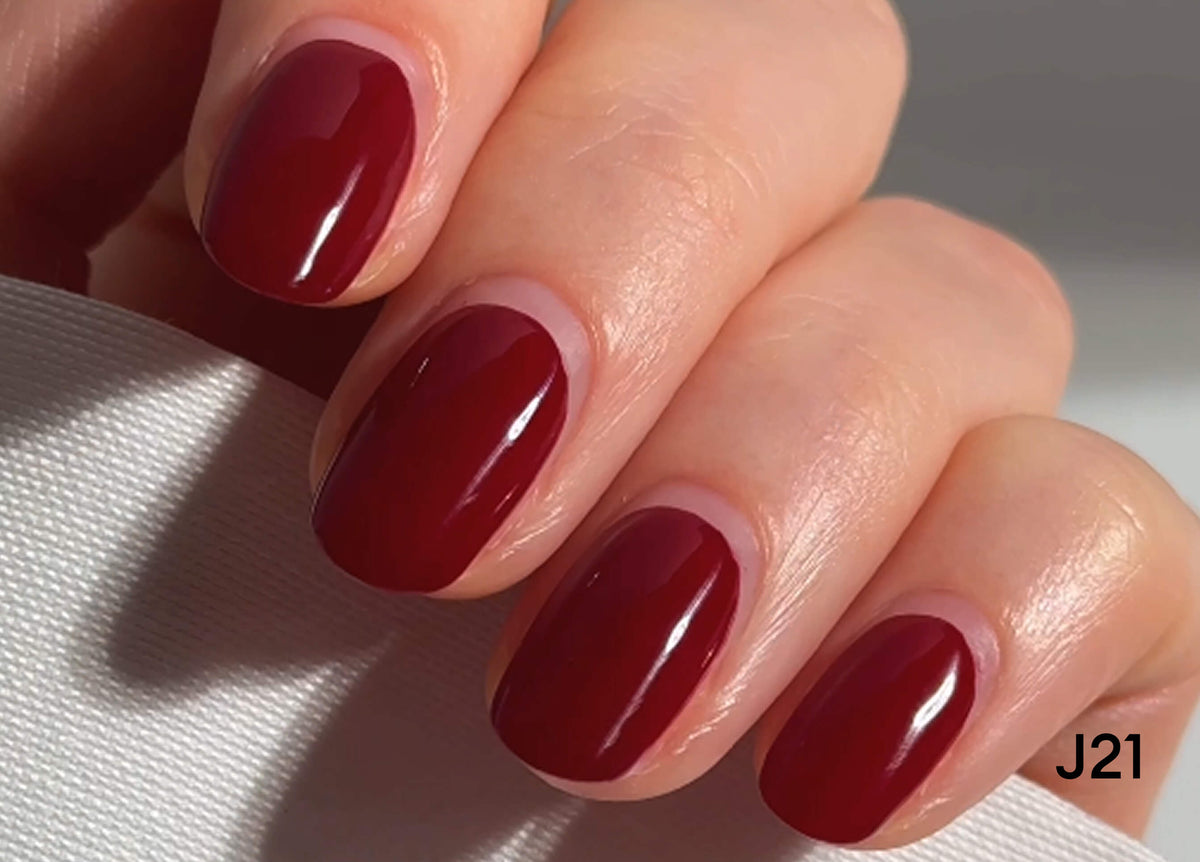 A close-up of a hand with neatly manicured nails painted in a glossy deep red color. The nails are short to medium length, and the skin tone is fair. The code J21 appears in the lower right corner.