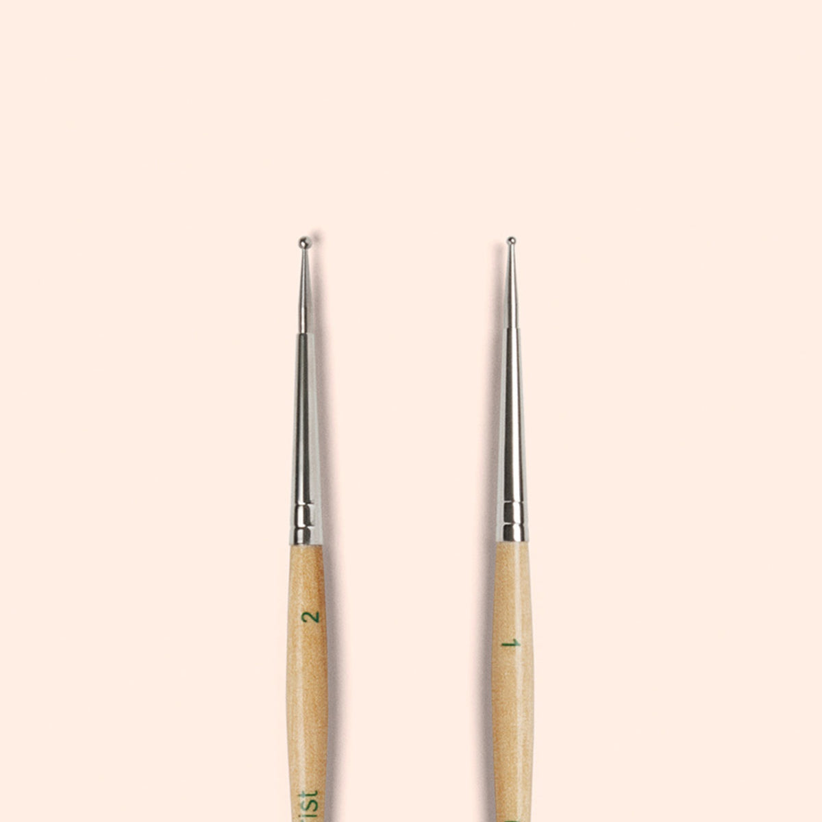 Two Manucurist Dotting Tools with metal tips and FSC wood handles are shown standing upright side by side on a light beige background, ideal for creating precise nail art designs.