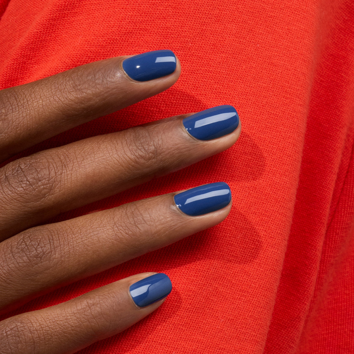 Une main aux ongles soigneusement manucurés, peints en "Midnight" par Manucurist, repose sur un tissu rouge vif, créant un contraste de couleurs éclatant.