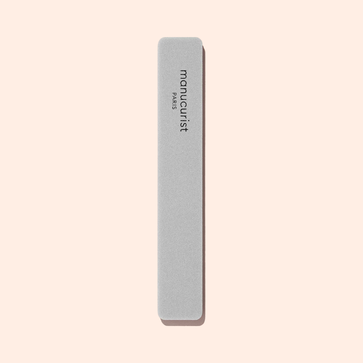 A rectangular gray Manucurist Nail buffer sponge with rounded edges is placed vertically on a light beige background, perfect for smoothing the nail plate and prepping your manicure.