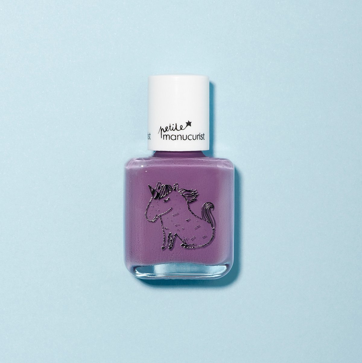 Un flacon de vernis pour enfants Manucurist Lily the Unicorn violet éclatant sur fond bleu clair, orné d&