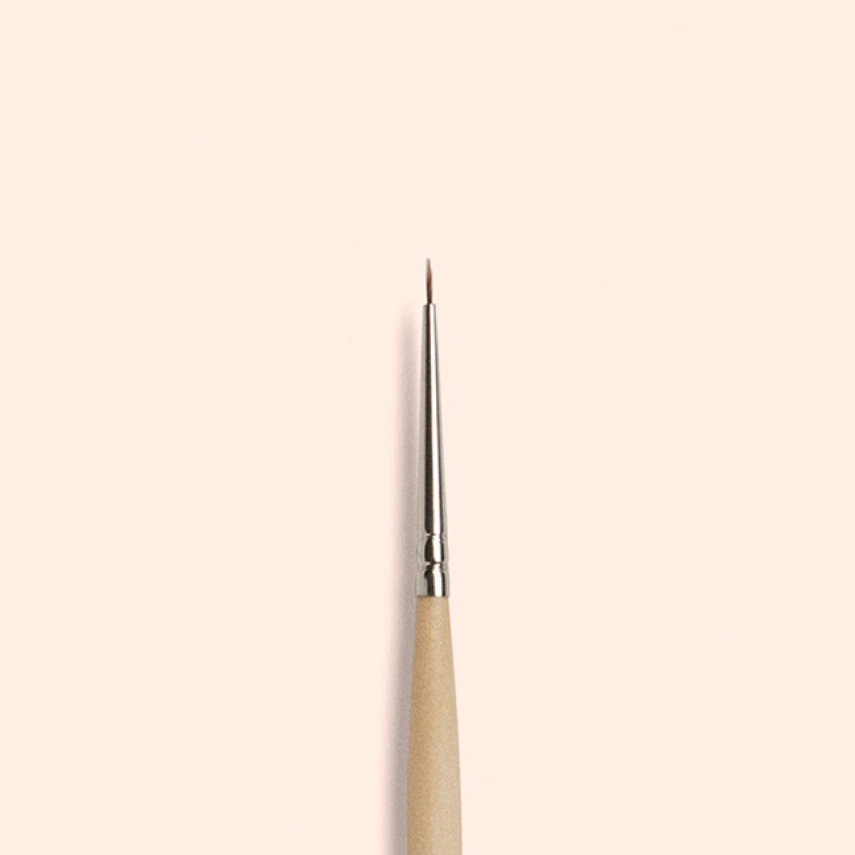 The Manucurist Fine Tip Brush, made with vegan synthetic bristles, a wooden handle, and a silver ferrule, stands vertically against a light beige background—perfect for creating precise nail art.