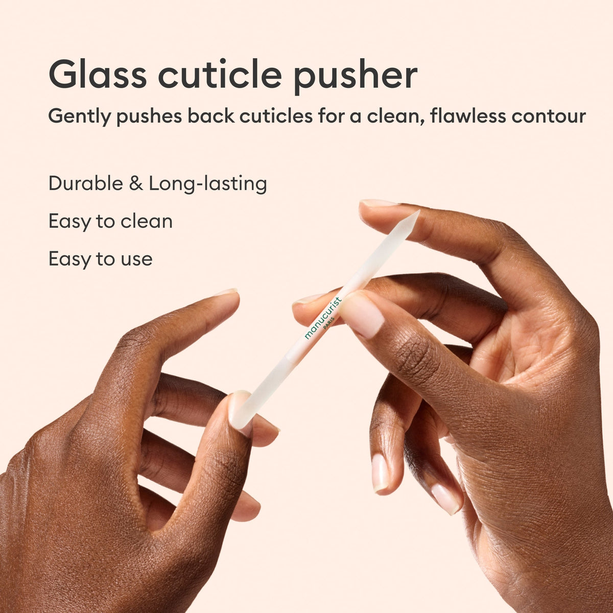 Two hands hold the Manucurist Glass Cuticle Pusher against a beige background. This professional tool gently shapes nail contours, is durable, long-lasting, easy to clean, and effortless to use.