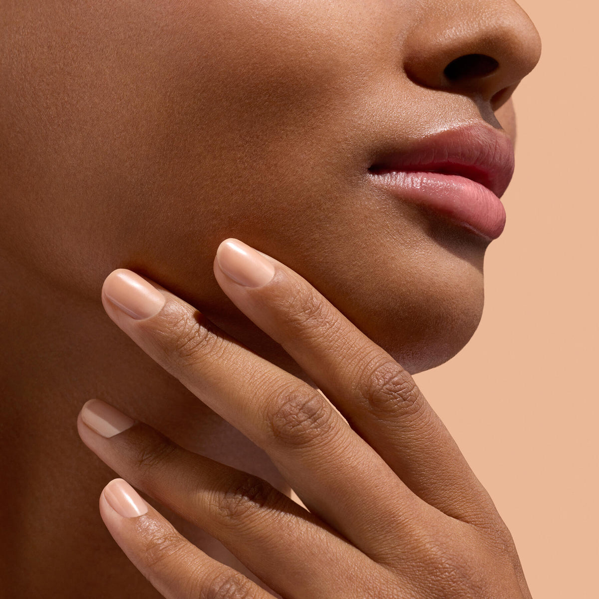 A close-up of a person’s lower face and hand, showing smooth skin, natural lips, and neatly manicured nails—highlighting meticulous nail care with Manucurist Active™ Smooth 02—set against a beige background.