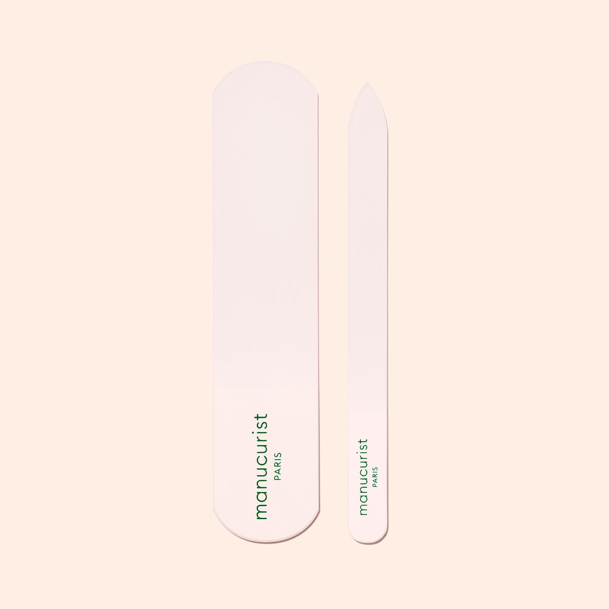 A pink nail buffer and file, both labeled "manucurist PARIS" in green, lie side by side on a beige background—ideal to pair with the Manucurist-us Glass Foot File for soft, smooth skin.