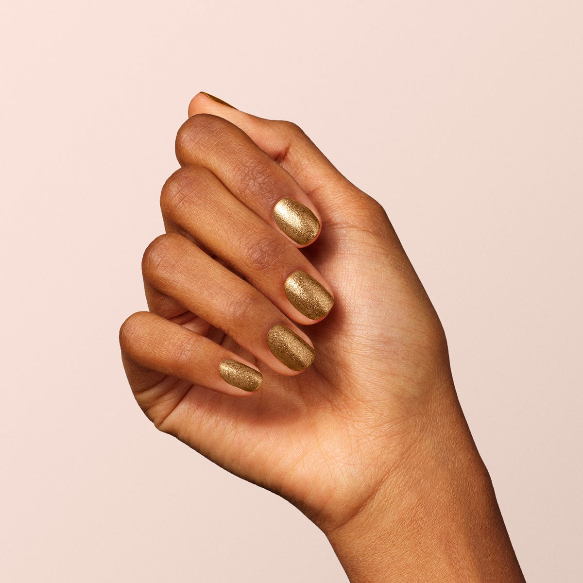 A hand with medium brown skin, fingers slightly curled inward, displays nails painted in Manucurist&
