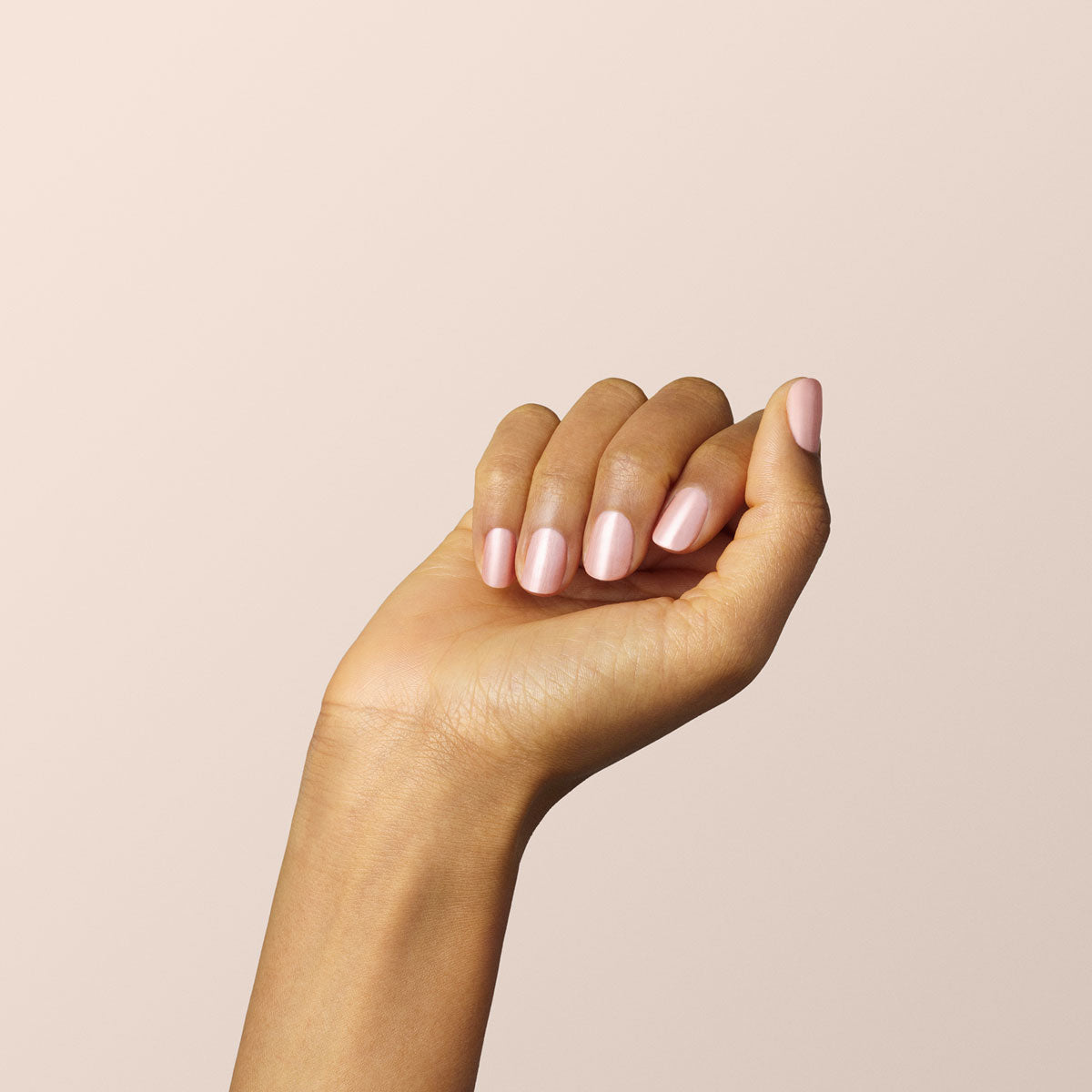 A hand with light brown skin is shown against a beige background, fingers gently curled to display neatly manicured nails painted in Manucurist&