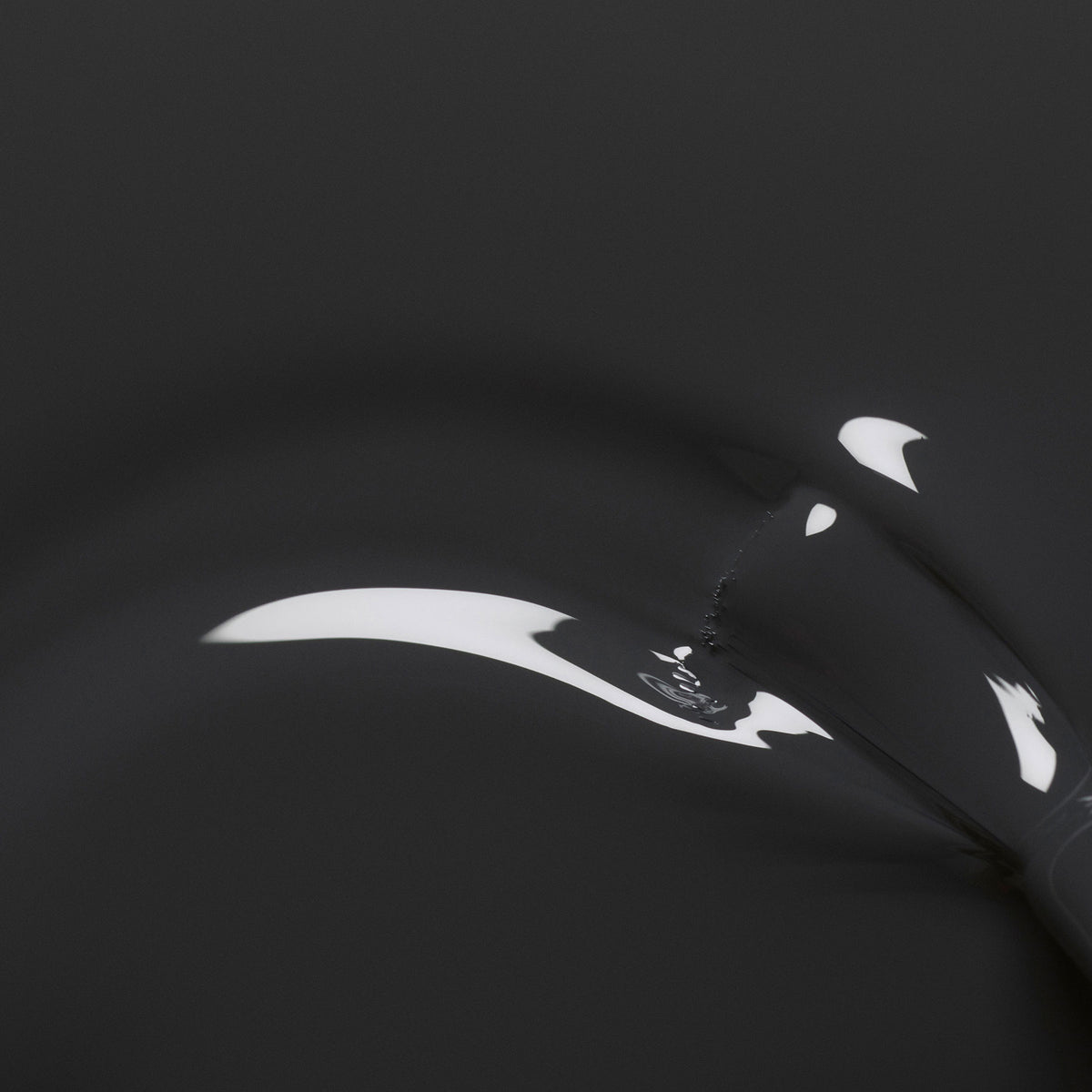 A close-up of Anthracite by Manucurist shows a black, glossy surface with smooth curves and white reflections, evoking dark grey nail polish for an abstract, minimalist effect.