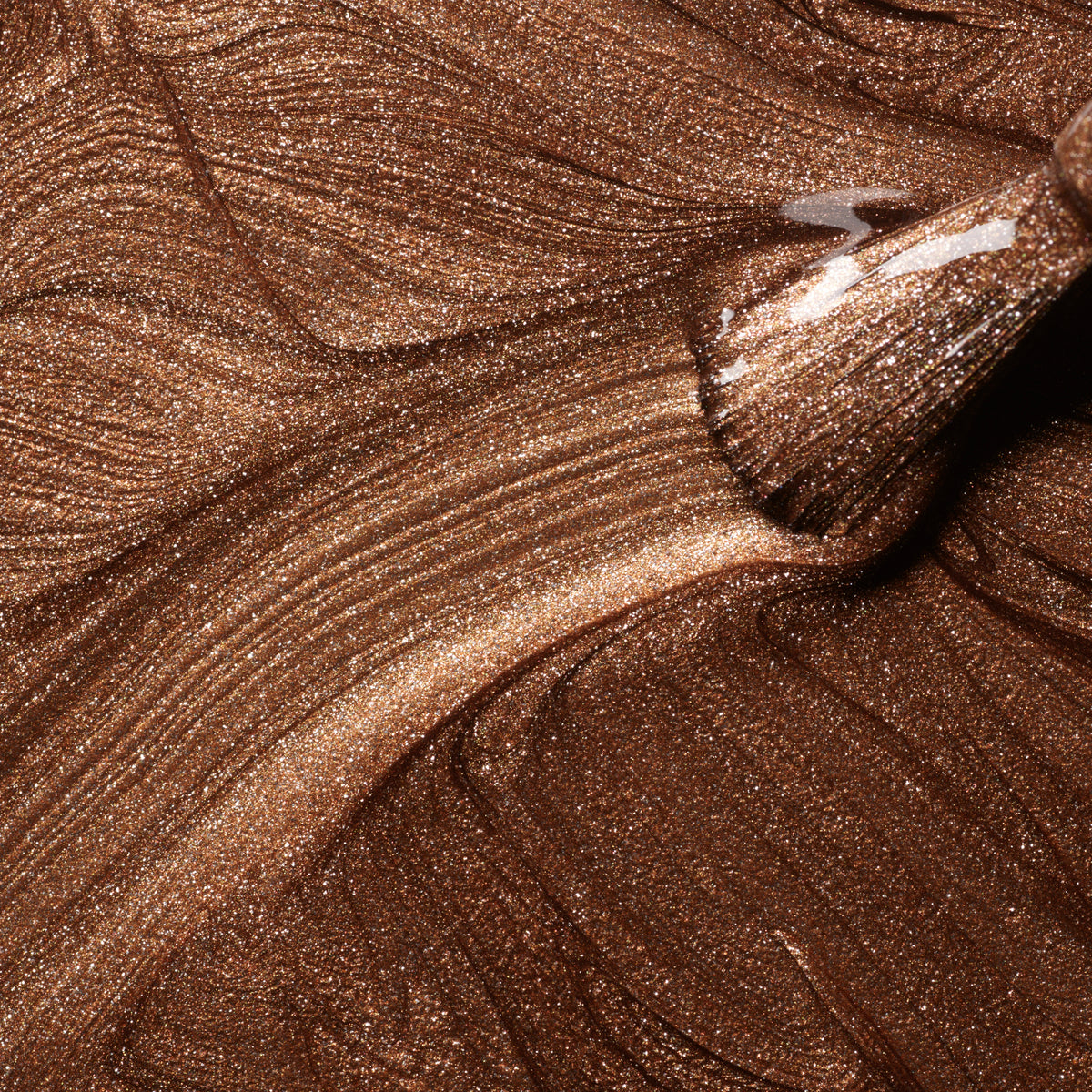 A close-up shows a Manucurist Bronzé nail polish brush applying shimmering, metallic bronze and copper gel polish in smooth strokes.