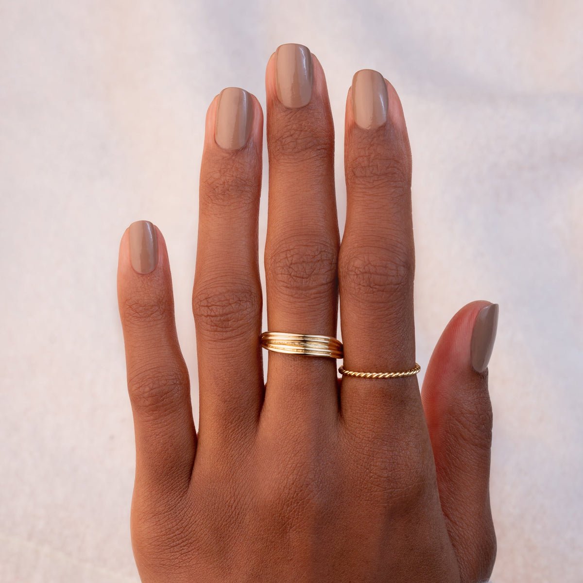 A hand with brown skin and neatly manicured nails painted in Manucurist&