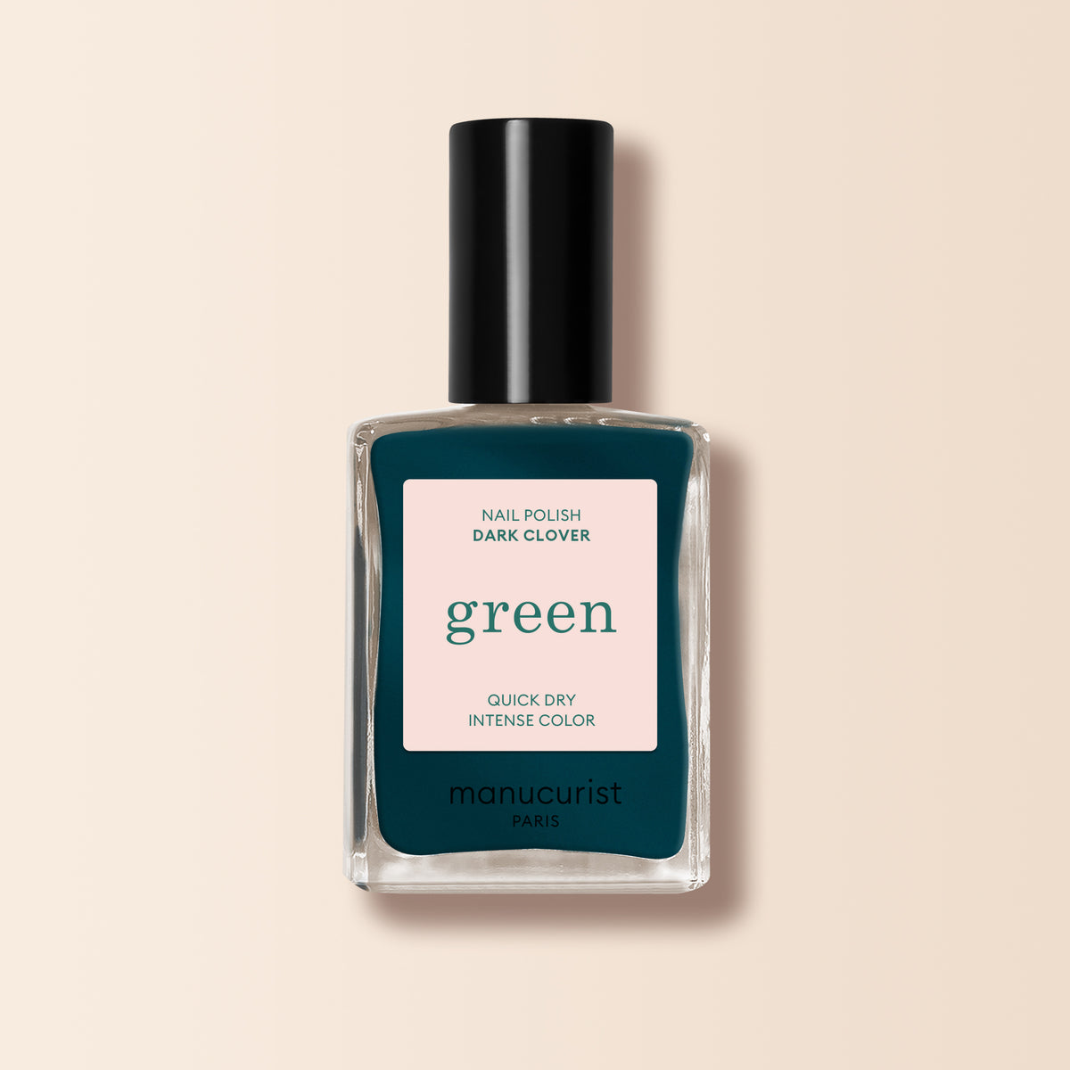 Un flacon de vernis à ongles Manucurist Dark Clover, avec un bouchon noir et une teinte vert foncé, est posé sur un fond beige clair. L&
