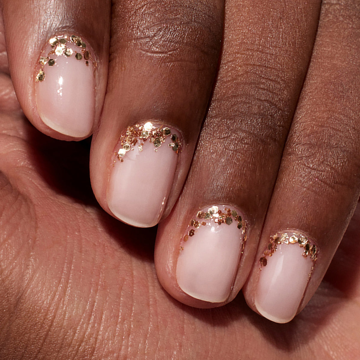 Gros plan sur une main aux ongles rose naturel arborant un Nail Art élégant, avec des touches de paillettes biodégradables Rose Gold Manucurist près des cuticules pour un look subtil et écoresponsable.