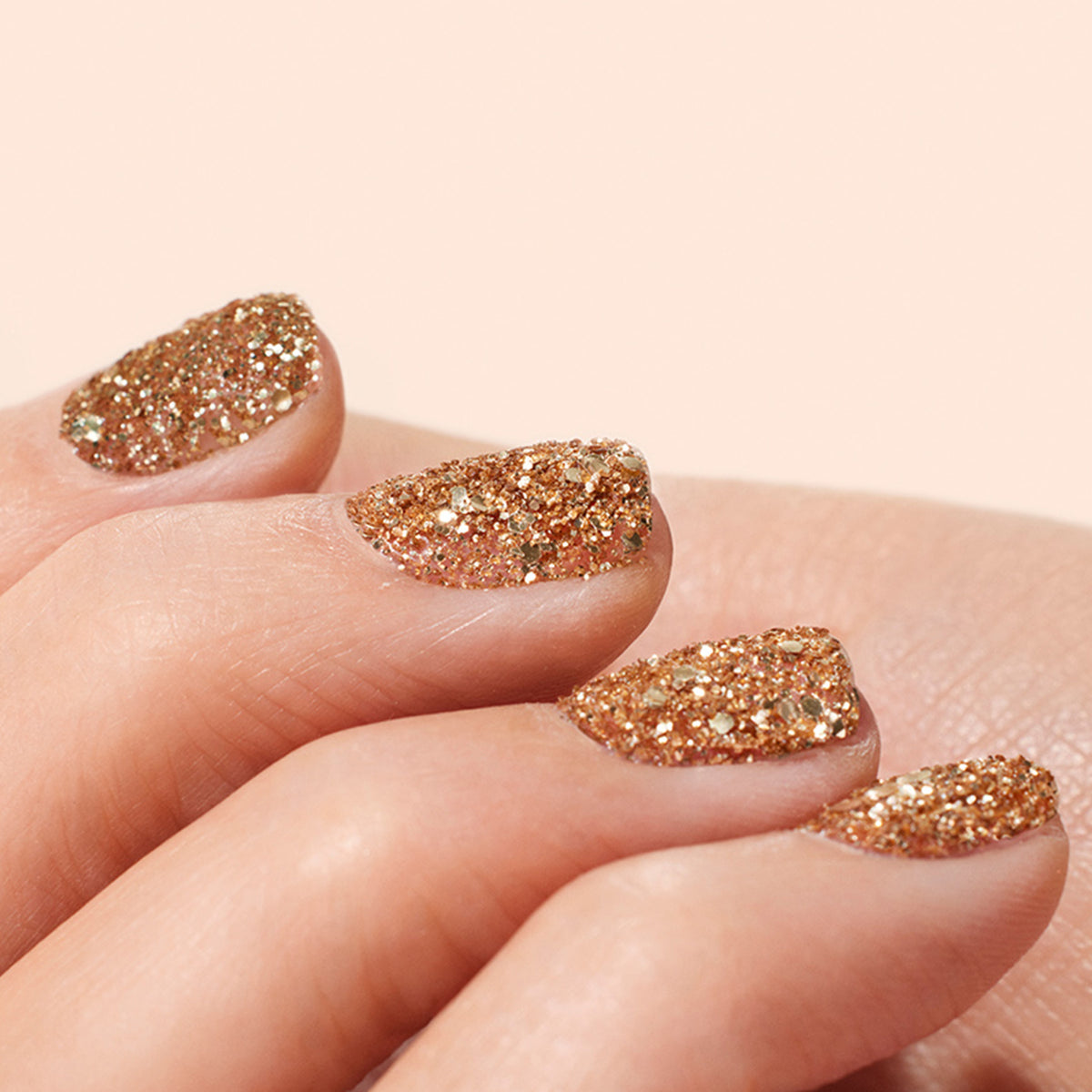 Gros plan sur une main aux ongles vernis avec les paillettes biodégradables Rose Gold de Manucurist, sur un fond doux et neutre.