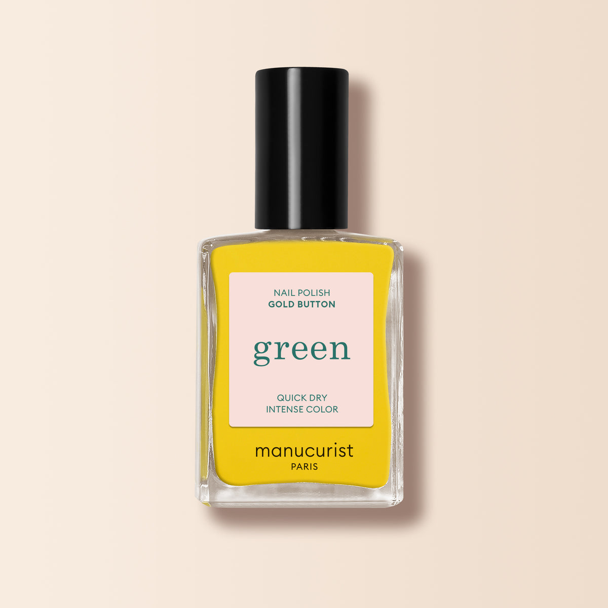 Un flacon de vernis à ongles jaune Gold Button de Manucurist avec un bouchon noir et une étiquette "couleur intense verte à séchage rapide", présenté sur un fond beige clair.