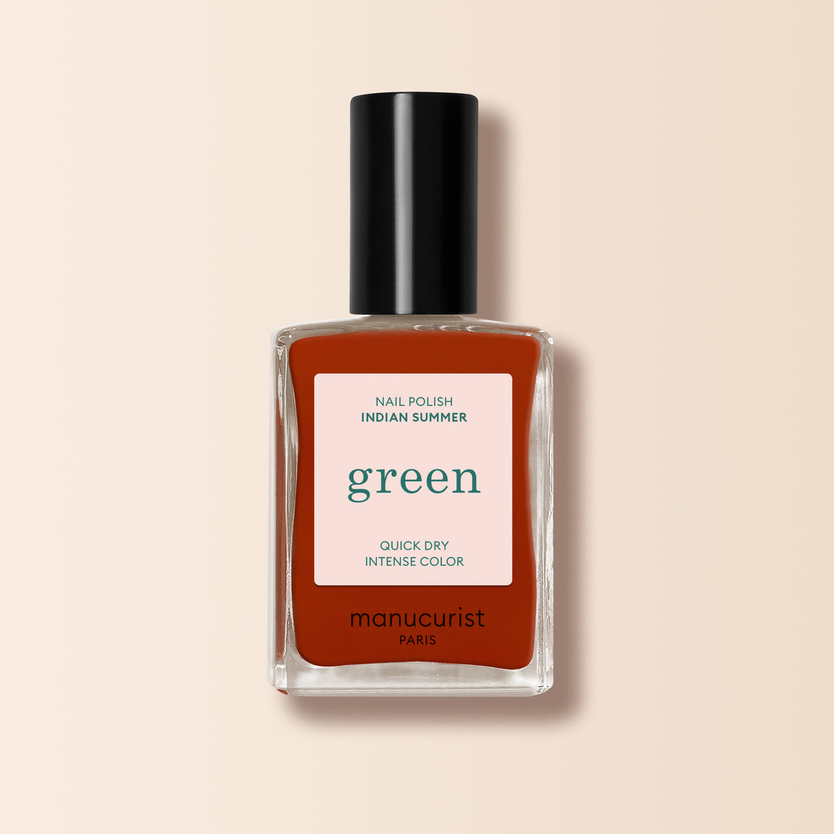 A bottle of Manucurist Indian Summer nail polish in brick red, from the Green™ range, comes in a rectangular glass bottle with a black cap and a label highlighting green, quick dry, and intense color on a light beige background.