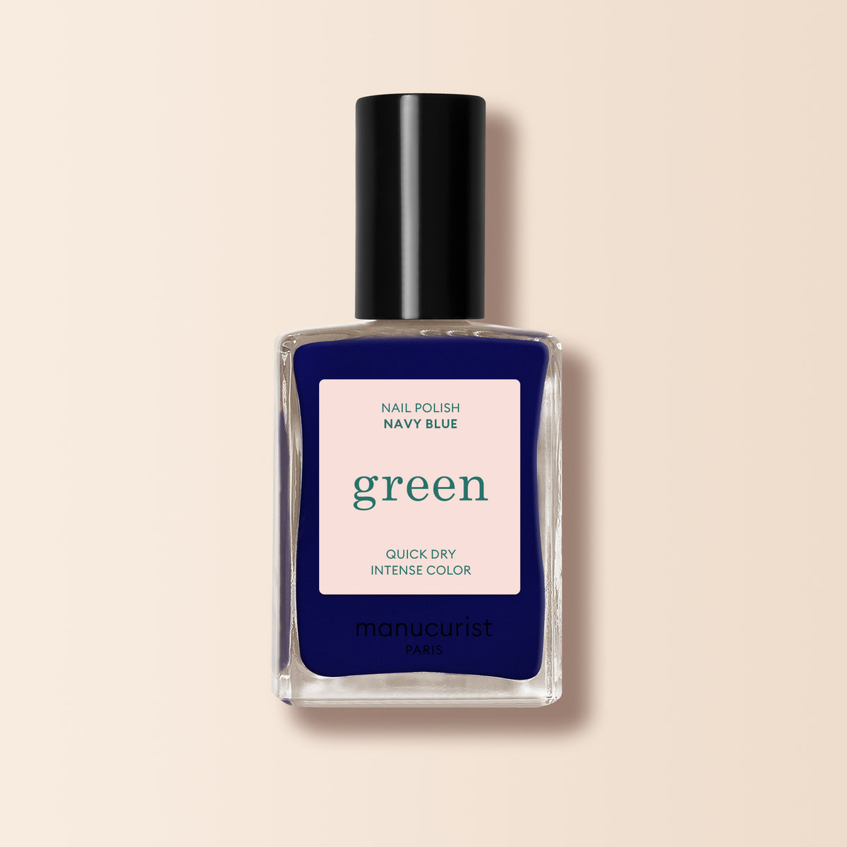 Un flacon de vernis à ongles Navy Blue de Manucurist de la gamme Green™, avec un bouchon noir. L’étiquette indique Nail Polish Navy Blue, Quick Dry Intense Color et manucurist Paris. Le fond est beige doux.