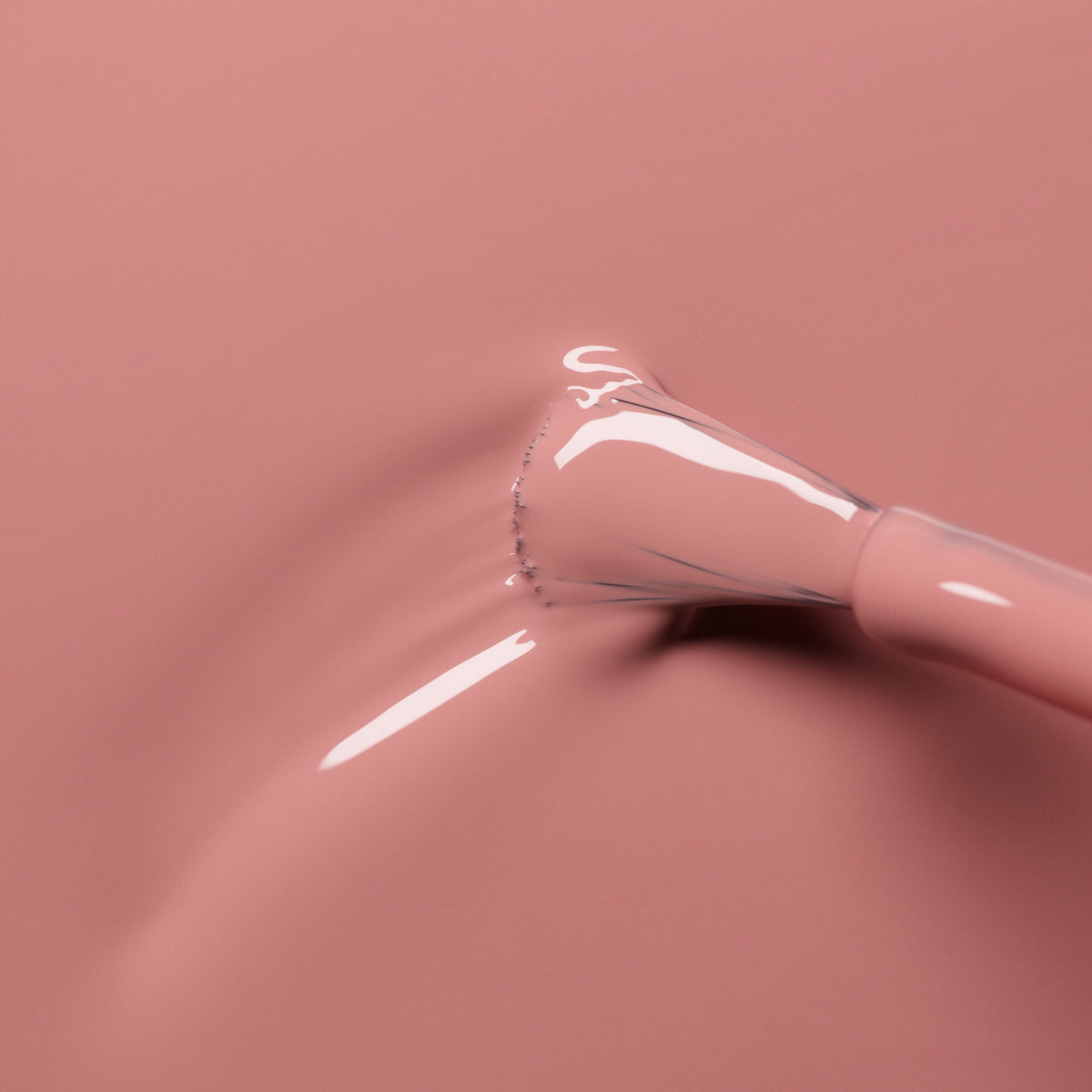 A close-up of a nail polish brush coated in Manucurist’s glossy Old Rose shade, with the smooth antique pink polish spreading across a matching surface.