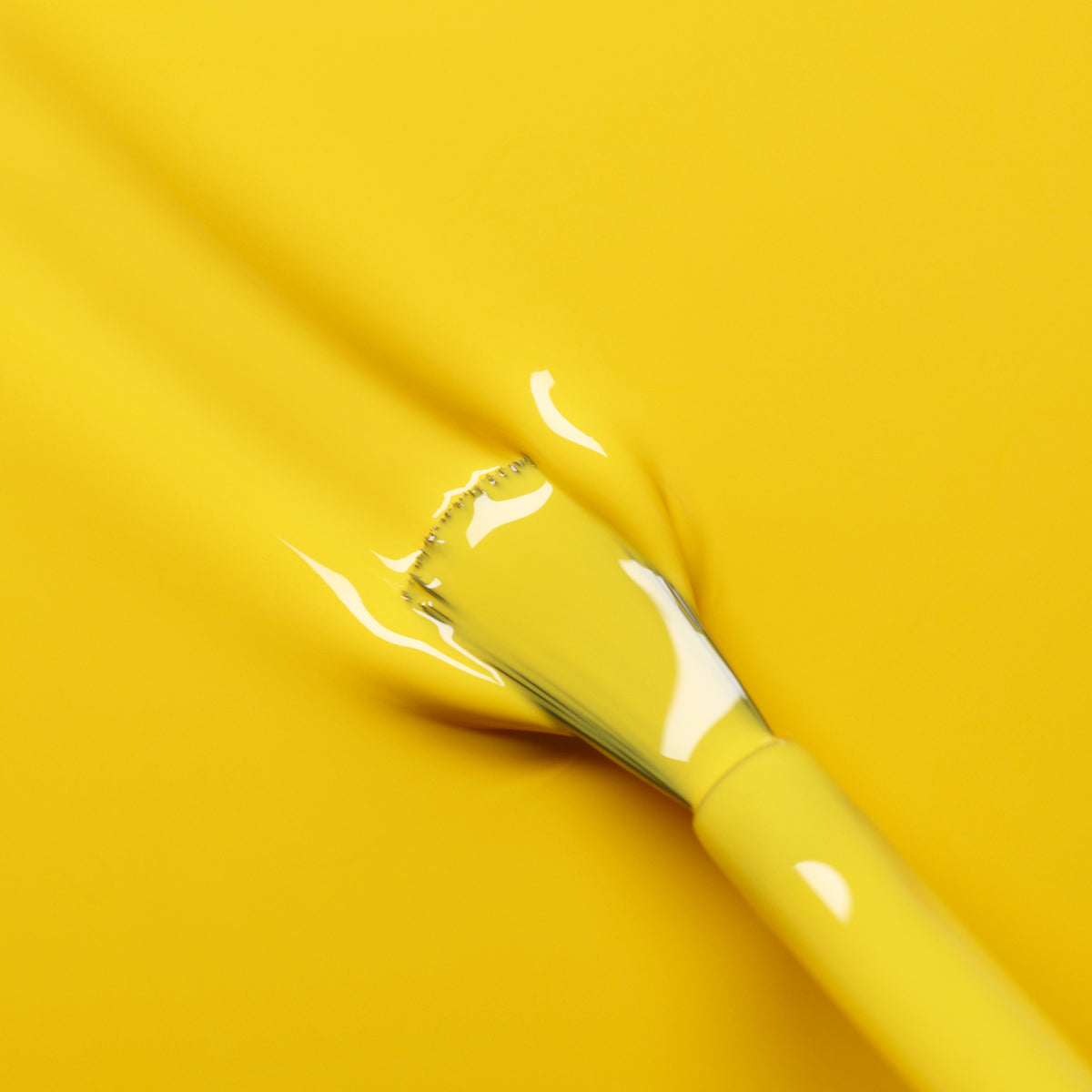 Un pinceau enduit de vernis Gold Button de Manucurist se fond parfaitement sur une surface jaune vif, créant un effet lisse et artistique.